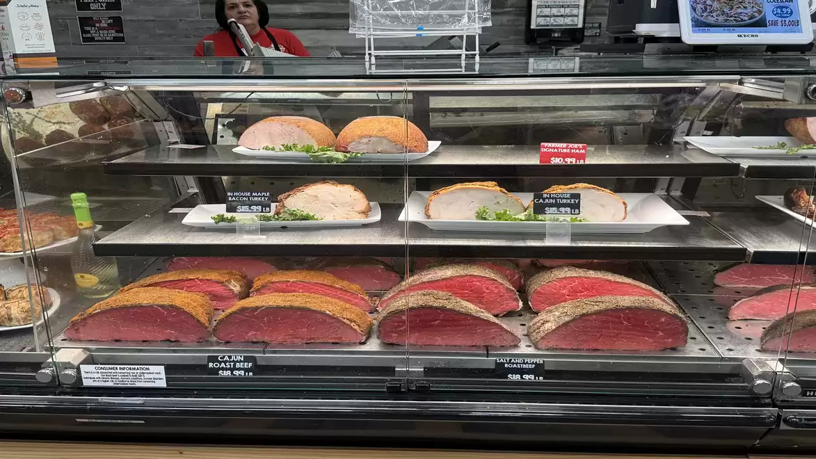 Deli counter in a supermarket displaying various meats like roast beef and roasts behind glass.