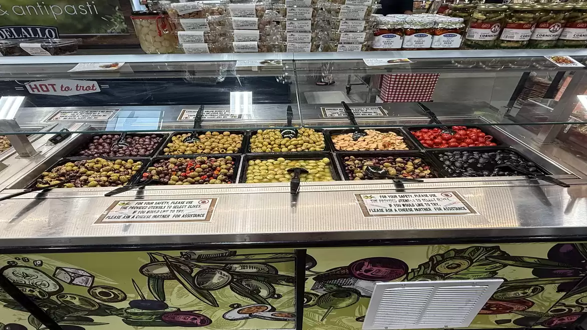 A delicatessen with a variety of antipasti such as olives, peppers, and cheese in a refrigerated display.