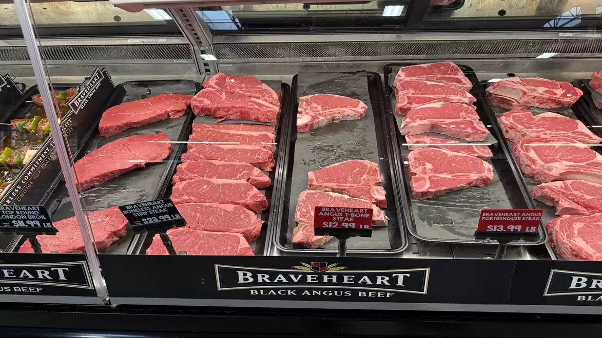 A refrigerated display case filled with various cuts of raw beef, including Braveheart Black Angus Beef.