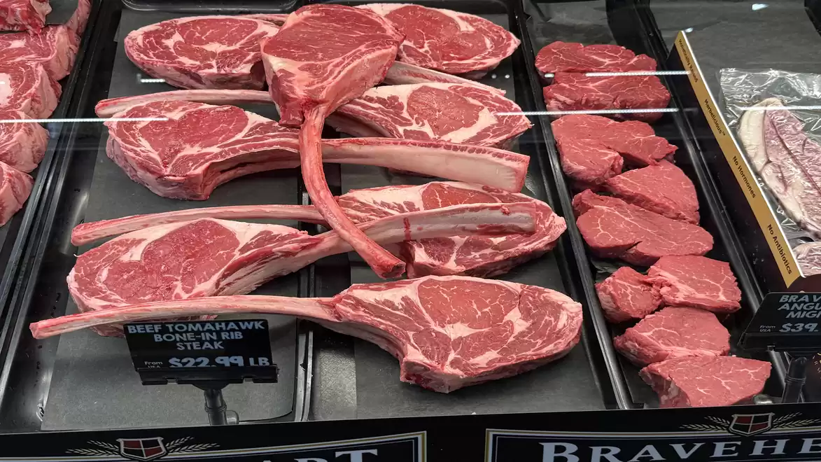 Display of raw tomahawk steak and other meats in a butcher shop.
