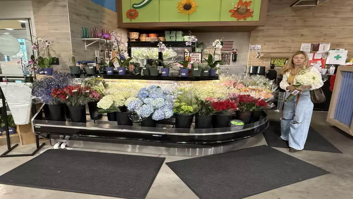 Flower shop with a diverse selection of bouquets and plants, a woman stands holding flowers next to it.