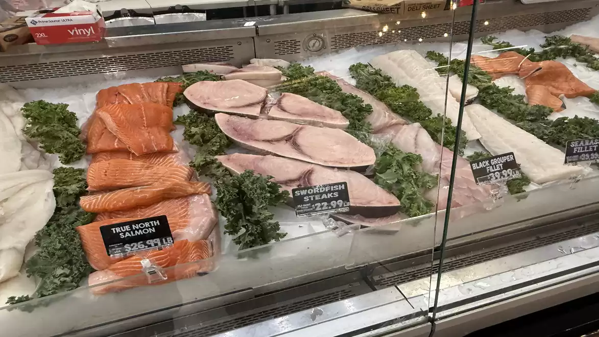 Fresh fish counter with a variety of fish fillets and herbs in a supermarket.