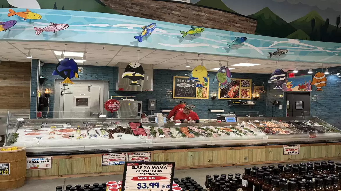 A fish store displaying a variety of fish and seafood on ice. Colorful fish decorations hang from the ceiling.