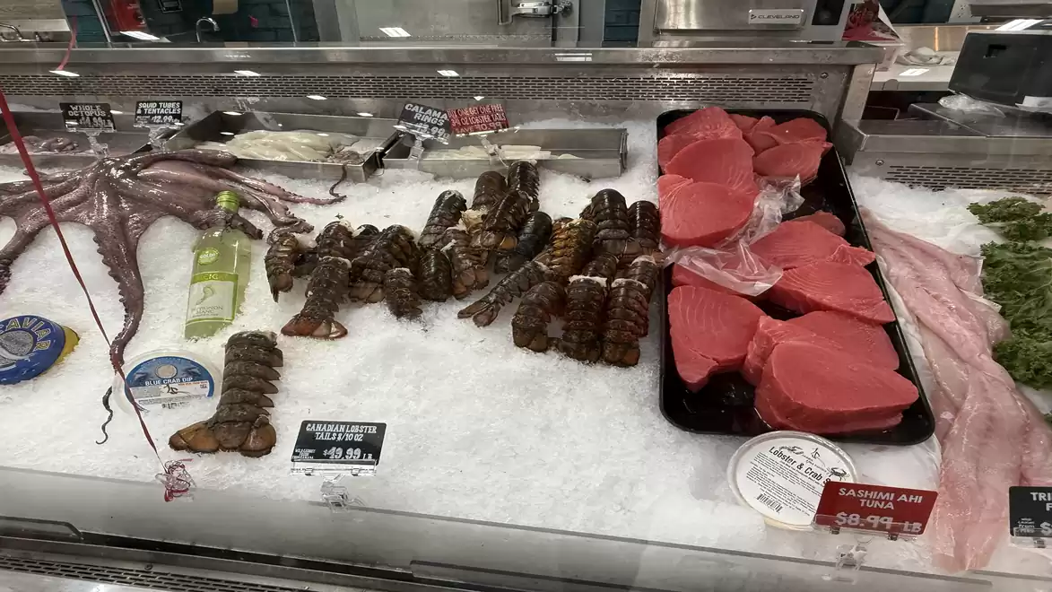 Fresh seafood display with lobster, octopus, and tuna steaks on ice in a supermarket.