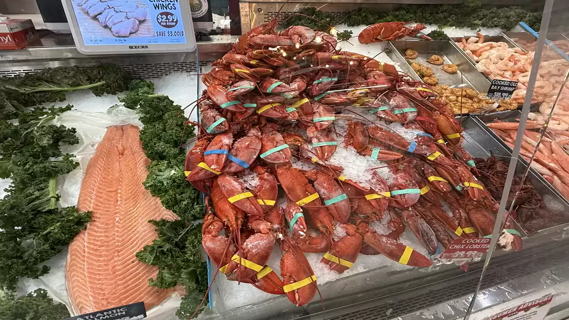 A fish market displays fresh seafood, including lobsters on ice, a salmon fillet, and shrimp, decorated with greenery.