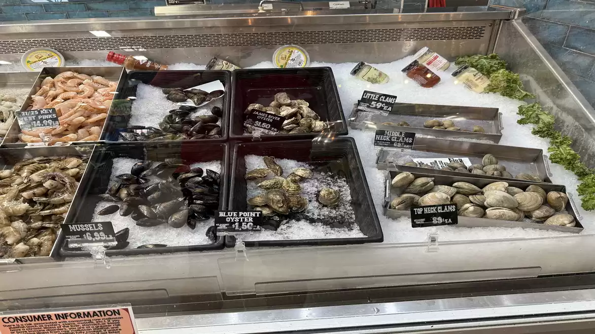 Fresh seafood and shellfish in a supermarket display, including shrimp, mussels, and oysters, presented on ice.
