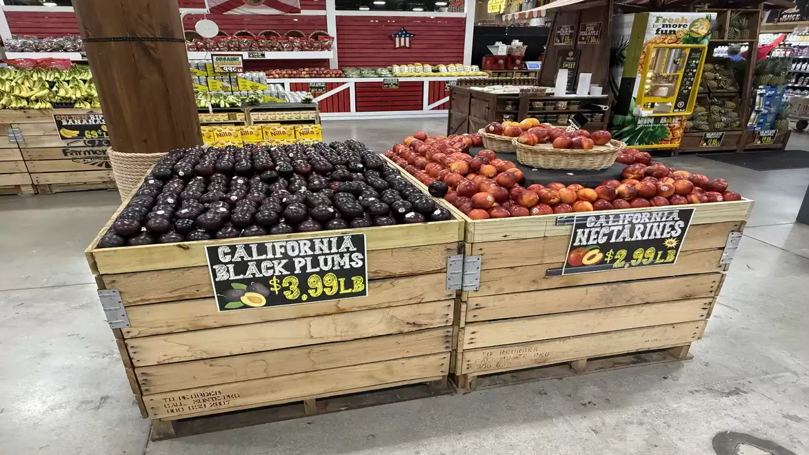 A fruit stand in a supermarket displays crates of California black plums and nectarines. Each crate has a price sign reading $3.99 per pound.