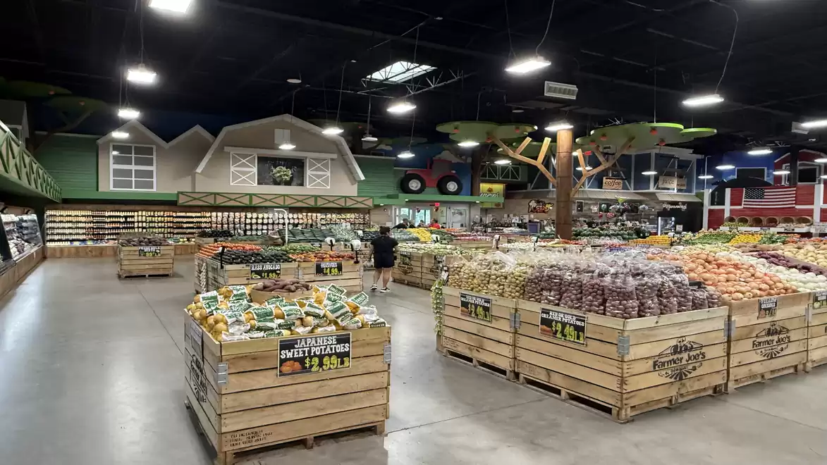 Interior of a large grocery store with wooden crates full of fresh produce such as fruits and vegetables. Farmhouse decorations in the background and high ceilings with artificial daylight.