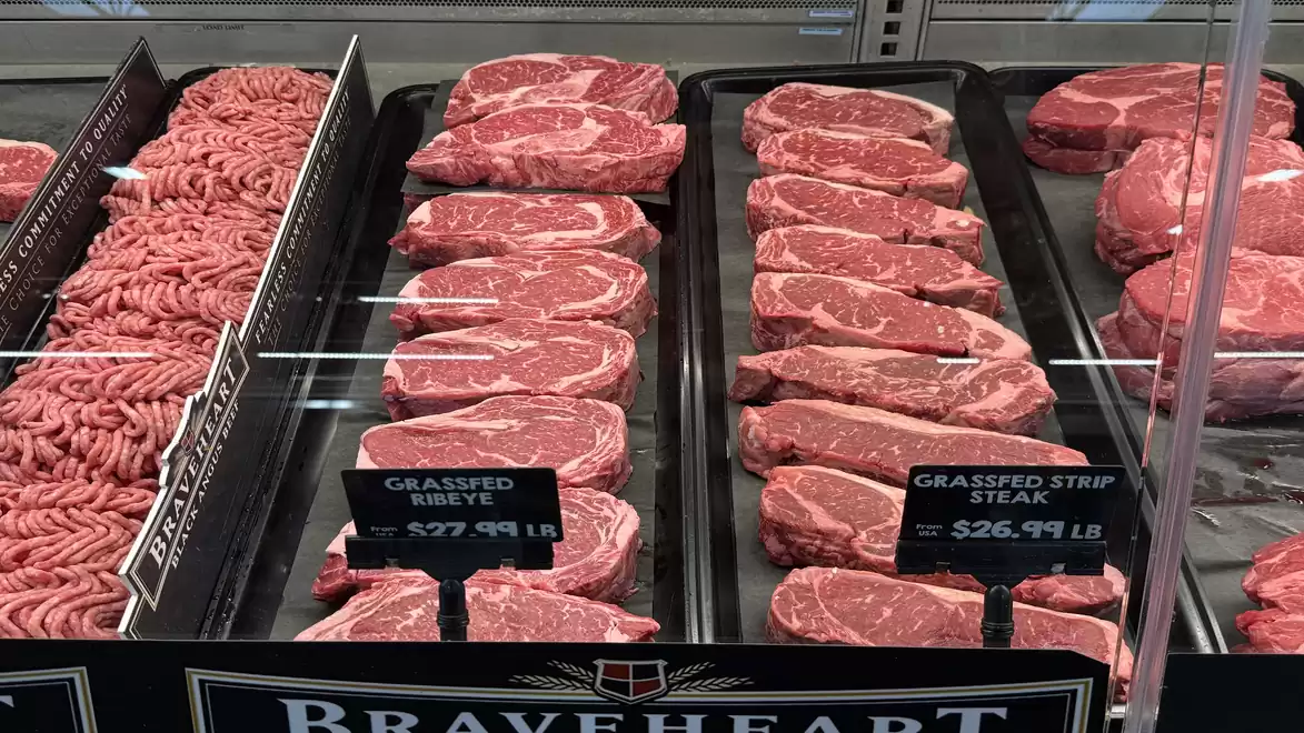 Close-up of various types of meat in a meat counter, including ground beef and beef steaks with price tags.