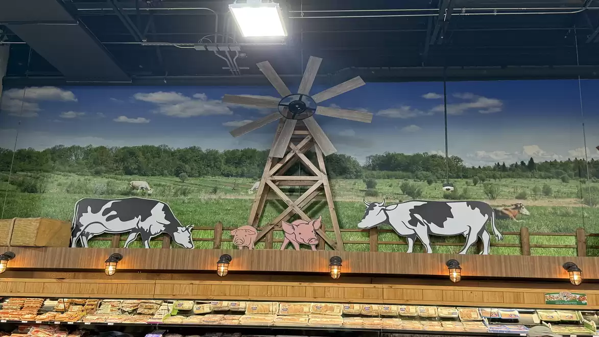 Supermarket decor with a farm theme, featuring a rural scene with a windmill, cows, and a pig.