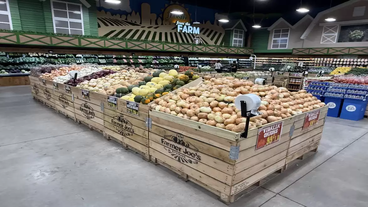 Large market area in a supermarket with wooden crates filled with fresh fruits and vegetables, surrounded by shelves with additional products.
