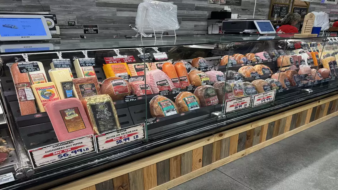 A deli counter in a supermarket with a wide selection of various meats and cheeses.
