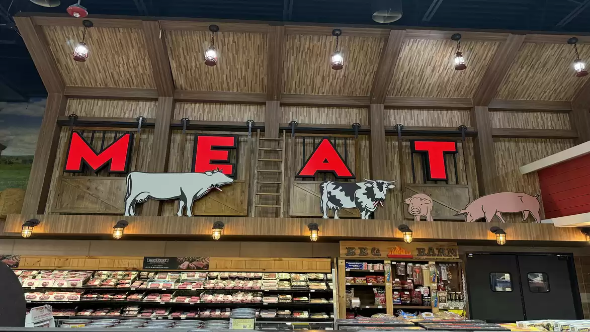 Supermarket meat section with large red letters MEAT and animal drawings on the wall.