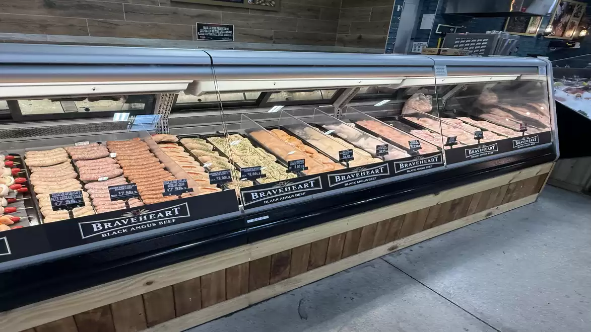 A refrigerated display case in a supermarket filled with various meat products. The products are neatly arranged and labeled.