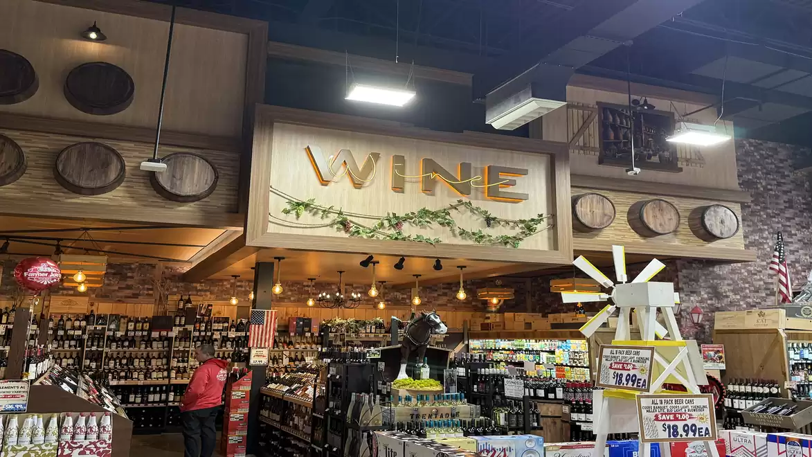A supermarket with an extensive wine section. Above the shelves hangs a large sign reading 'WINE'.