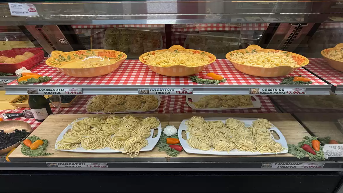 A store display shows various types of pasta in bowls and on plates presented on a red and white checkered cloth.