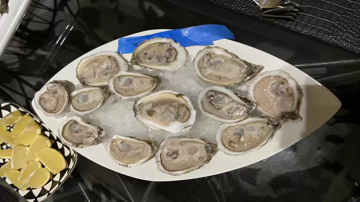 A plate of fresh oysters served on ice, accompanied by a bowl of lemon slices.