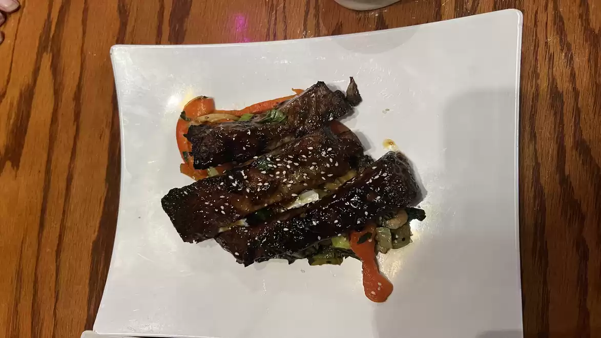 Grilled ribs with sesame on a white plate, served on a wooden table.