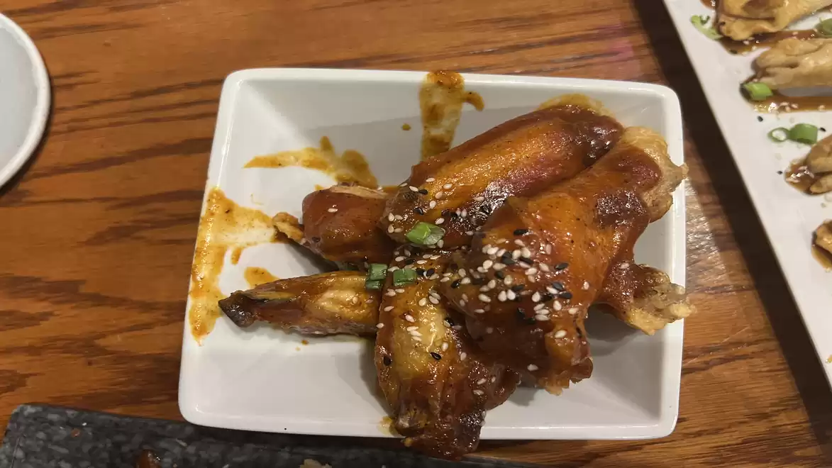A rectangular white plate with spicy chicken wings, garnished with sesame seeds and green onions, served on a wooden table.