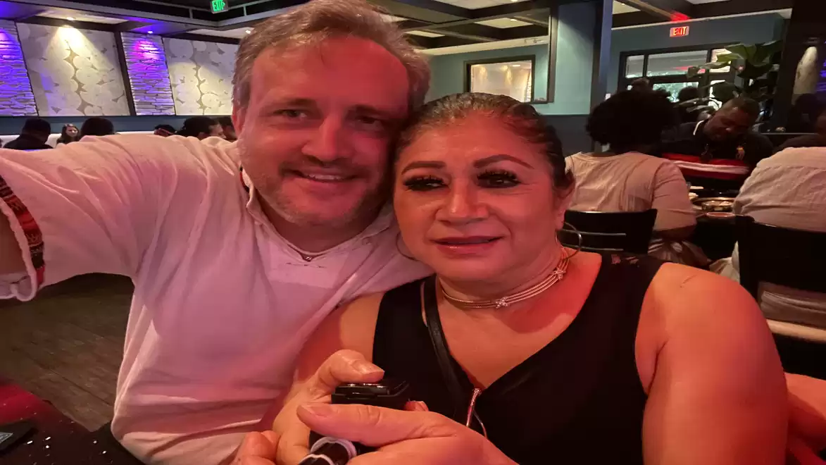 A man and a woman sitting together in a lively restaurant, smiling at the camera.