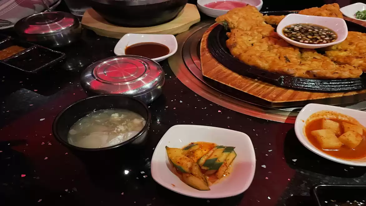 A table with a selection of Korean dishes, including pancakes, soup, and pickled vegetables.