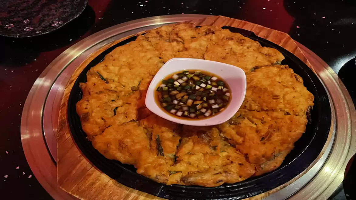 Korean pancake served on wooden platter with soy sauce.