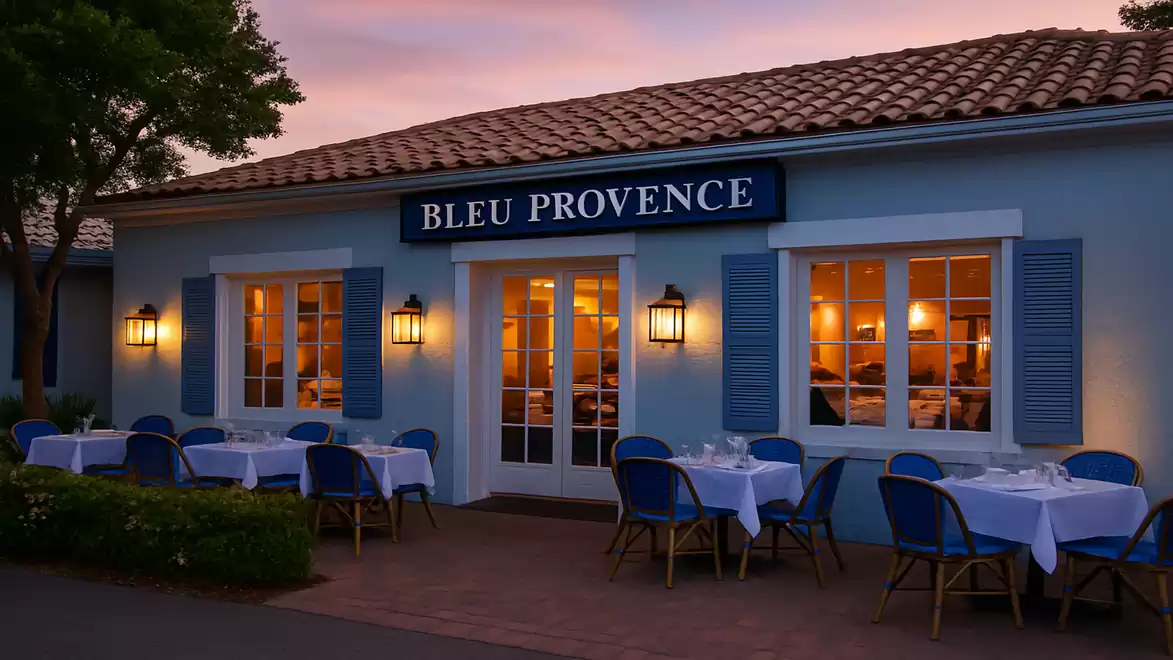 A charming French restaurant with a blue facade and set tables outside, illuminated at dusk.