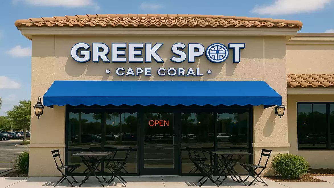 Exterior view of a Greek restaurant with a blue awning and tables in front of the entrance.