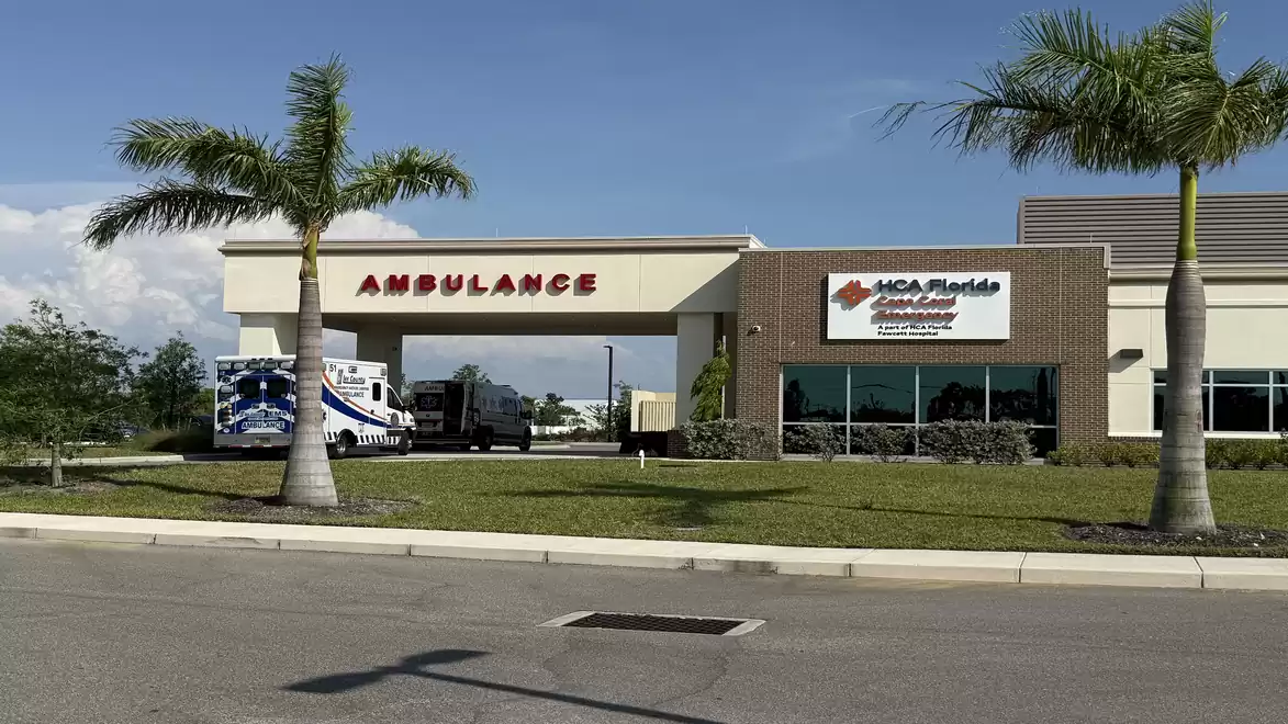 Ambulance entrance of a modern hospital with palm trees in the foreground.