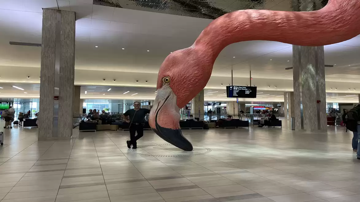 Giant flamingo sculpture in a modern airport with passengers in the background.