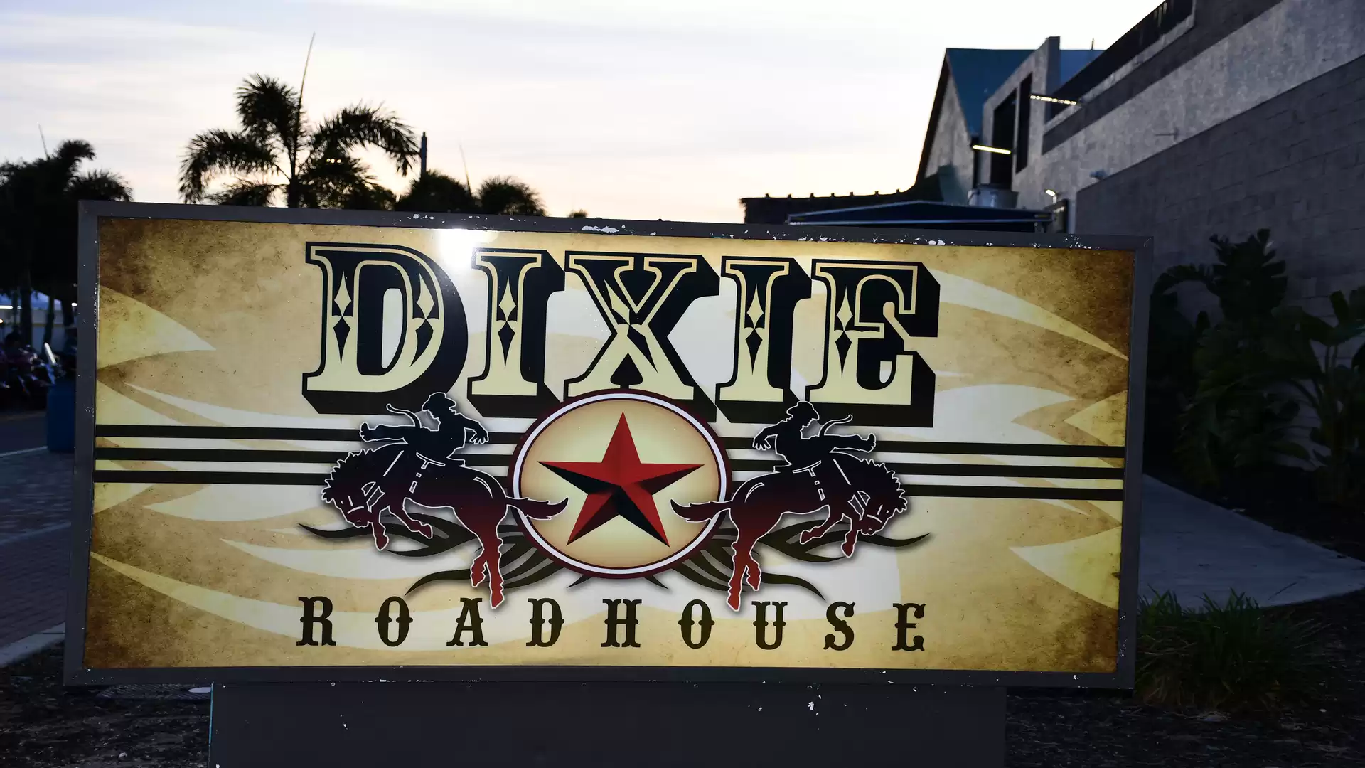 Illuminated sign in front of the building with the text 'Dixie Roadhouse' featuring a rustic Western design, lit during twilight.