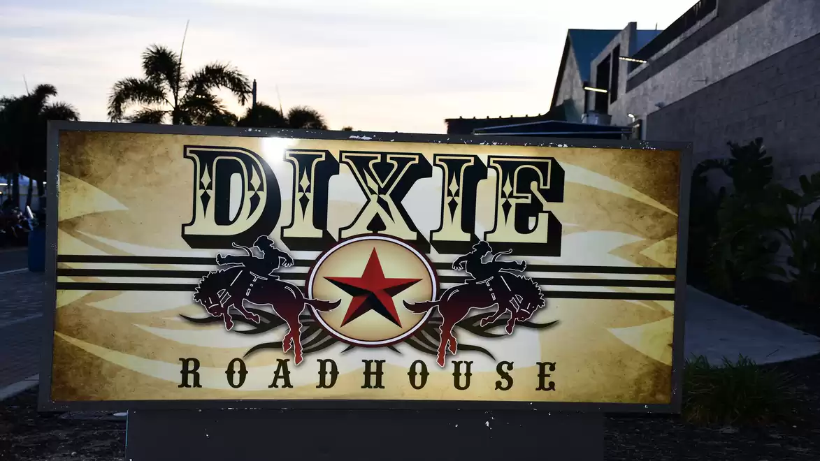 Illuminated sign in front of the building with the text 'Dixie Roadhouse' featuring a rustic Western design, lit during twilight.