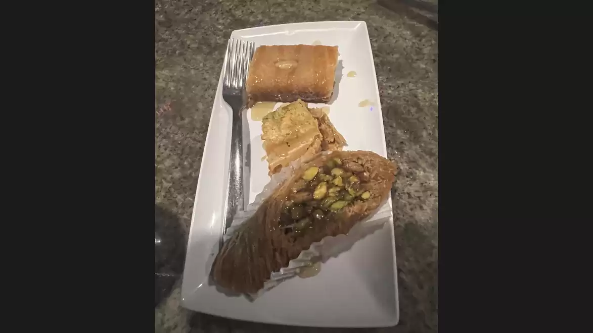A plate with different types of baklava on a granite surface. A fork lies next to the desserts.