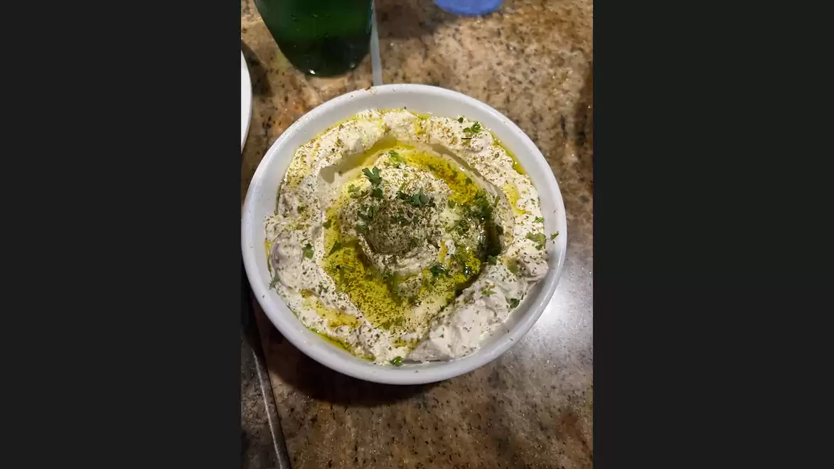 A bowl of hummus garnished with spices and olive oil on a table.