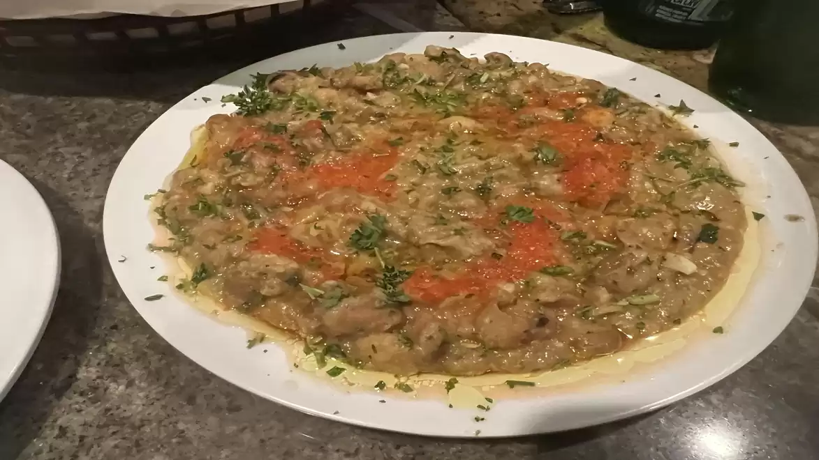 A plate of chopped raw fish garnished with red sauce and herbs.