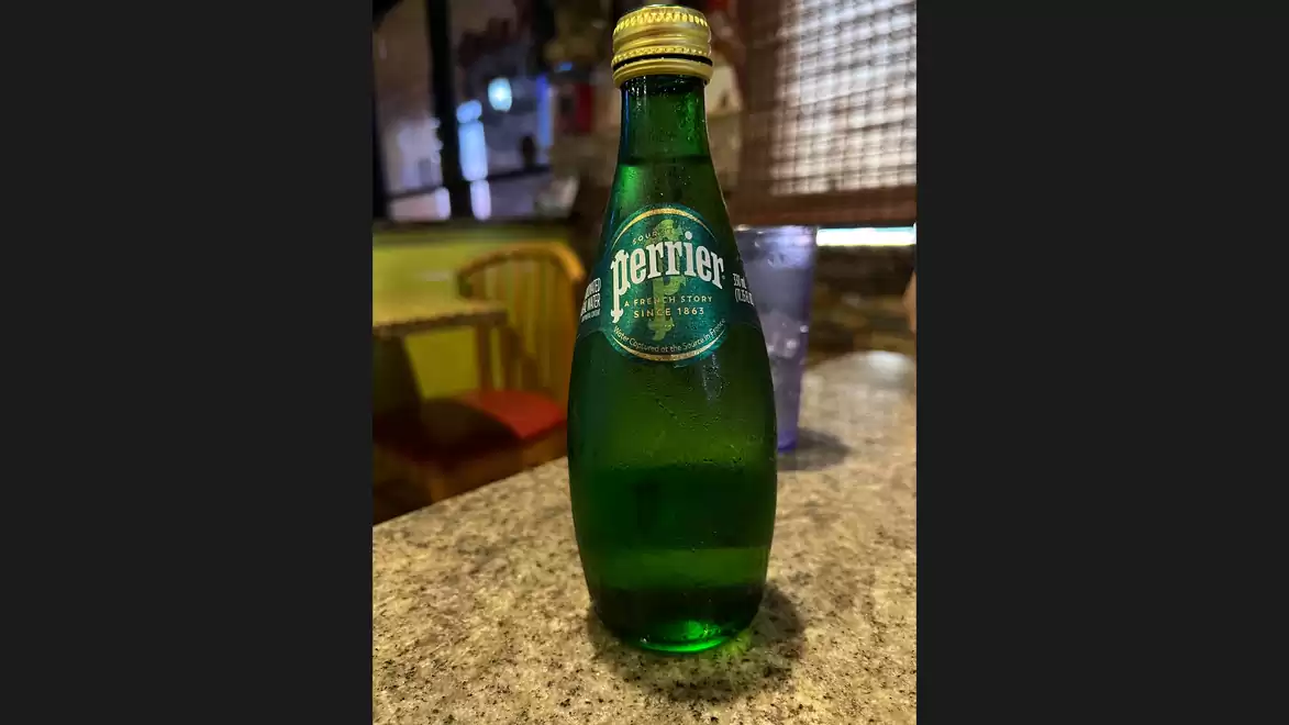 Green Perrier bottle on a table in a restaurant with a blurred background.