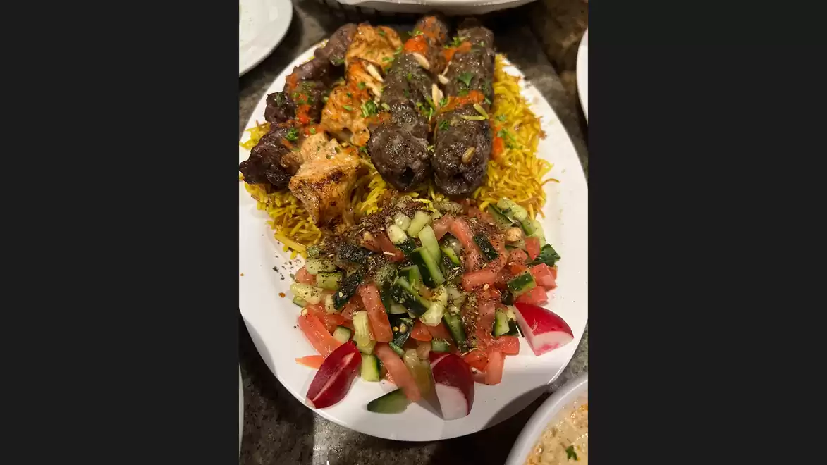 A plate with grilled meat skewers on saffron yellow rice, served with a colorful salad of tomatoes, cucumbers, and radishes.
