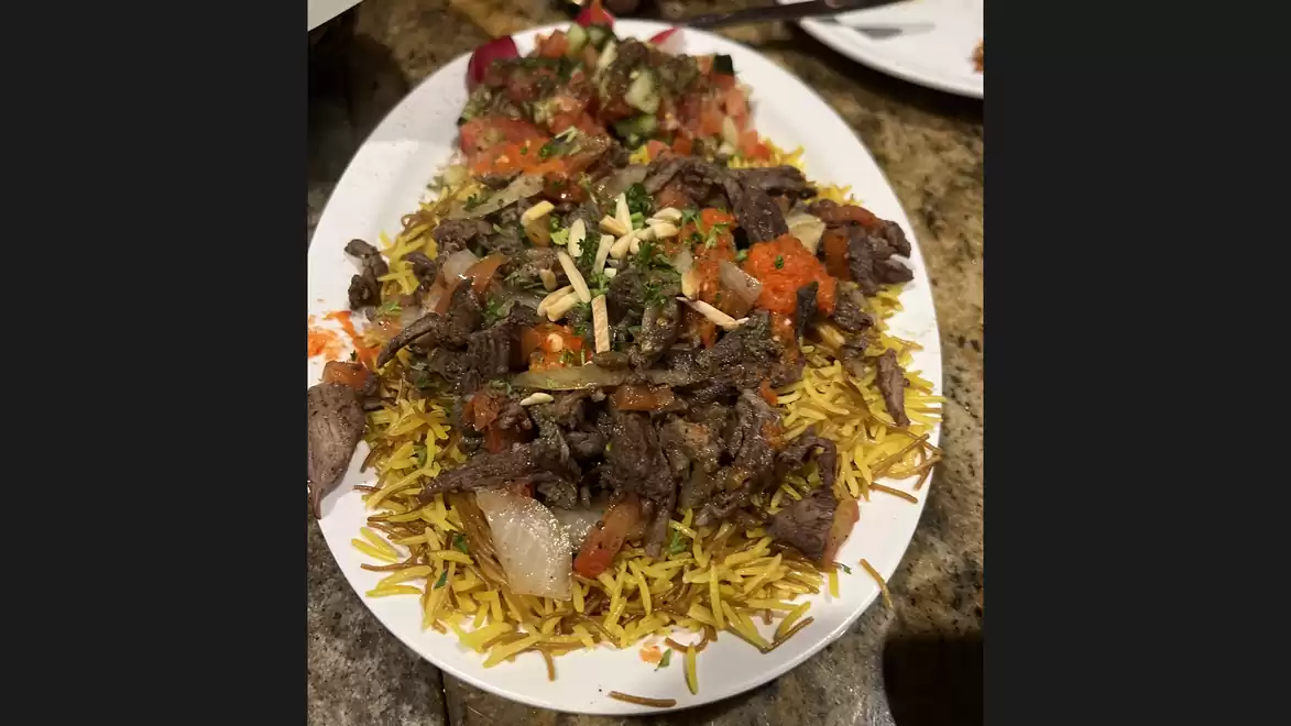 A plate of spicy rice topped with marinated meat and fresh vegetables.
