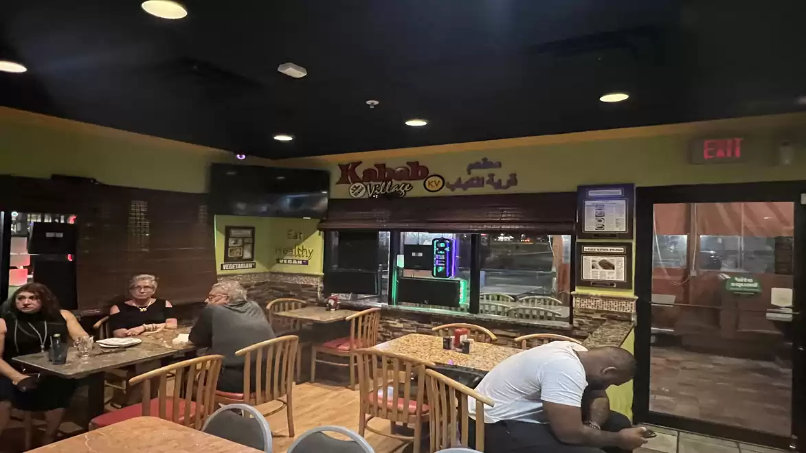 Interior view of a restaurant with empty tables and a few guests sitting at one table. Cozy lighting and décor.