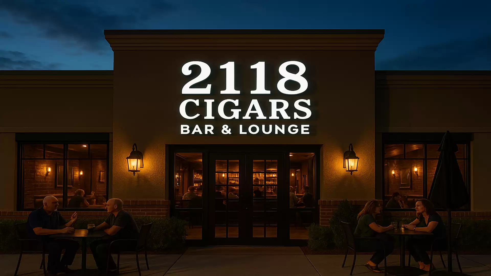 Evening view of a cigar lounge with the illuminated sign '2118 Cigars Bar & Lounge' and people sitting outside.