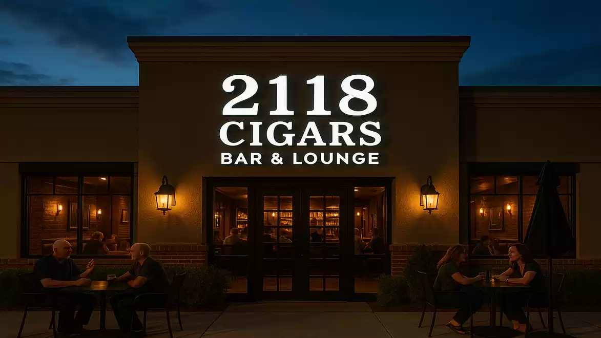 Evening view of a cigar lounge with the illuminated sign '2118 Cigars Bar & Lounge' and people sitting outside.