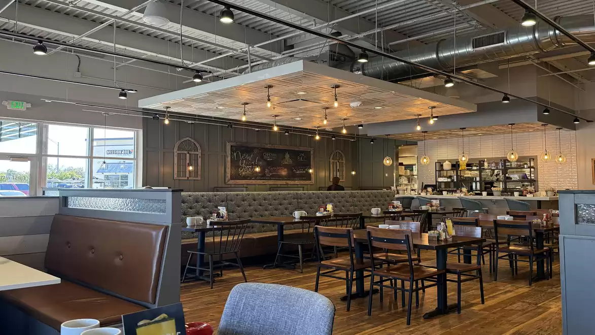 Modern cafe with wooden flooring, elegant pendant lights, and various seating options including tables and cushioned benches.