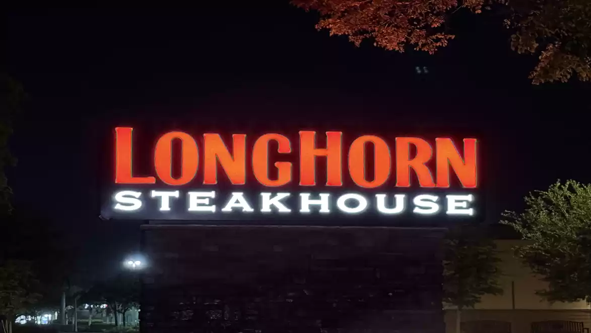 Illuminated LongHorn Steakhouse sign at night with trees in the background.