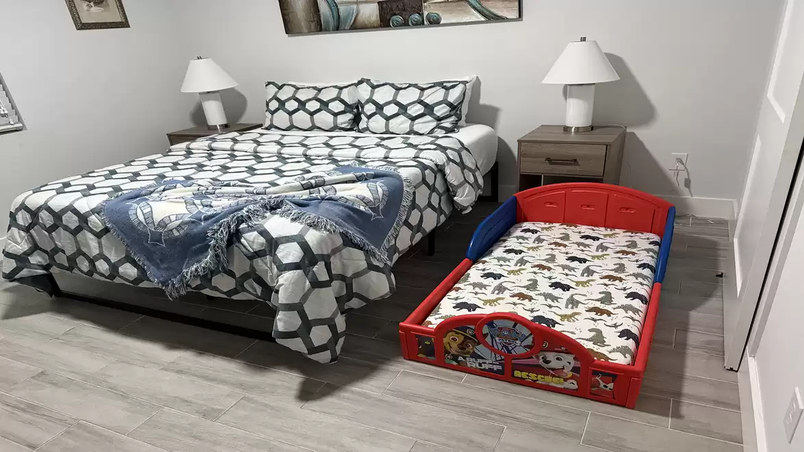 A bedroom with a large bed and a small toddler bed side by side. The bed linens have geometric patterns and the room is modernly furnished.