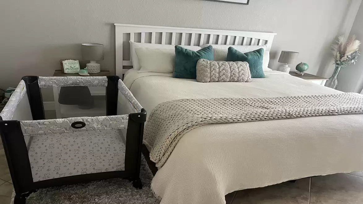 Modern bedroom with a large bed, decorated with green pillows, and a baby crib next to a nightstand.