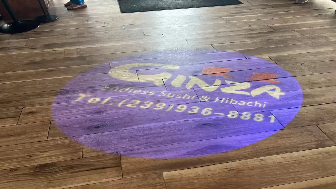 Wooden floor with projected logo of Ginza Endless Sushi & Hibachi with phone number.