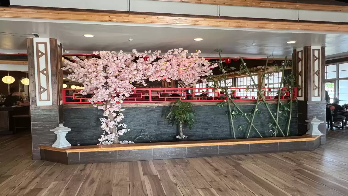 Interior view of a restaurant area featuring a decorative tree with pink blossoms, bamboo, and modern lighting.