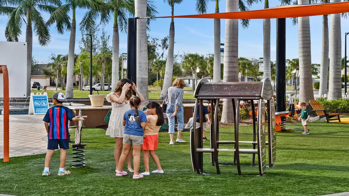 Children playing on a playground with palm trees in the background. A group of kids is talking and playing in sunny weather.