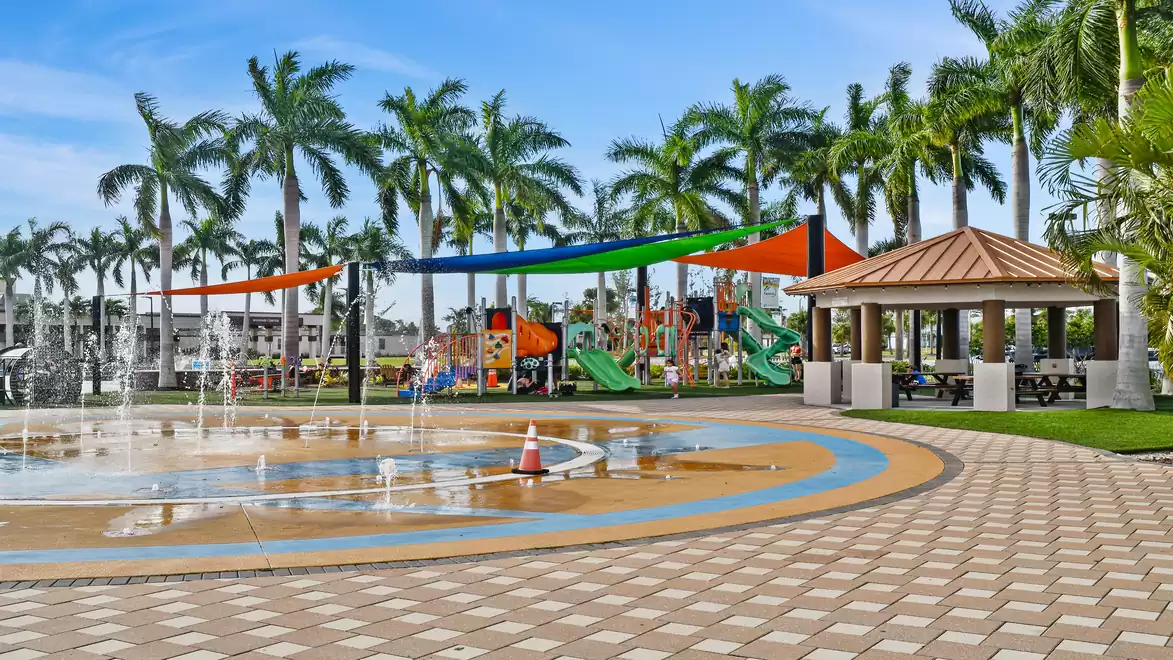Playground in a park with palm trees, colorful climbing frame, and water play area.