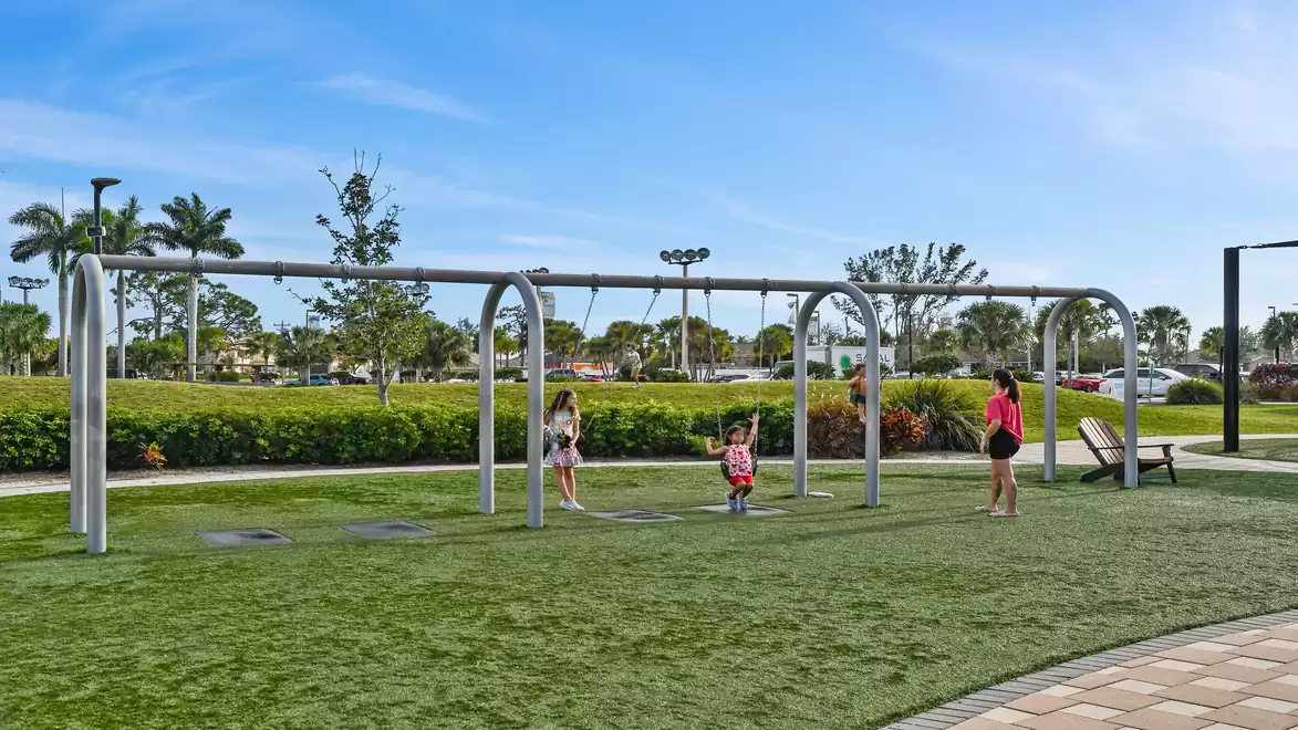 Three people playing at a modern playground with swings in a sunny park.
